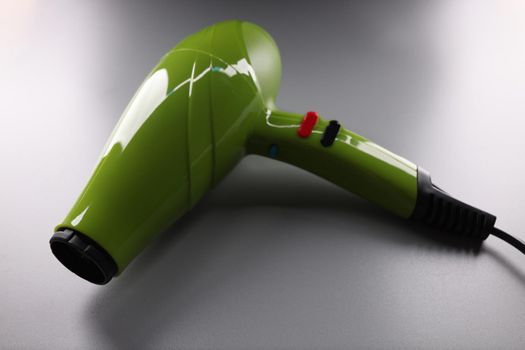 Green professional hair dryer lying on gray background closeup. Accessories for hairdressing concept