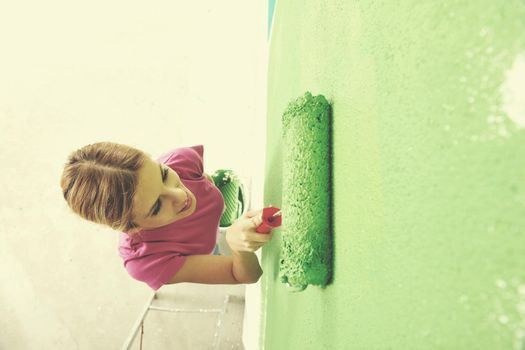 happy smiling woman painting interior white  wall in blue and green color of new house