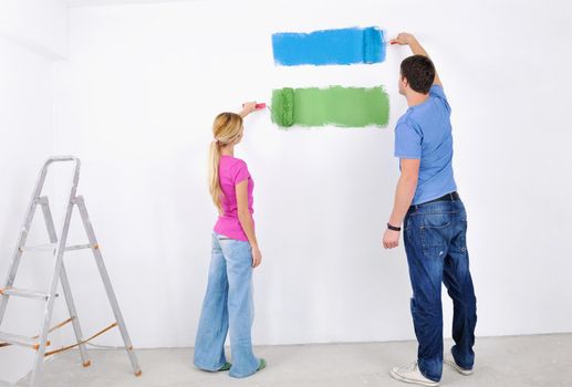 happy young couple paint in green and blue color white wall of their new home