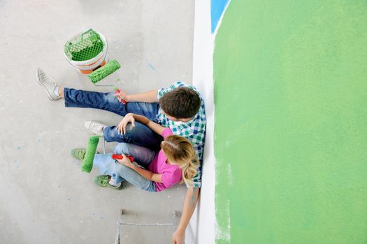 happy young couple relax after painting white wall in green and blue color in their new home