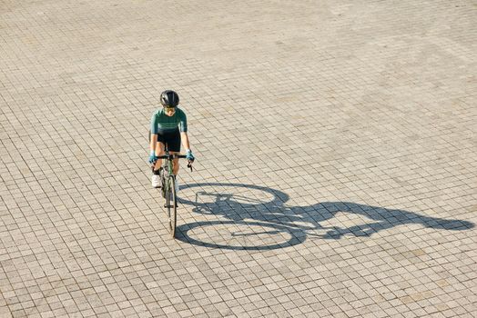 Aerial view shot of professional female cyclist in cycling garment and protective gear riding bicycle, training outdoors on a warm sunny day. Urban lifestyle, sports concept