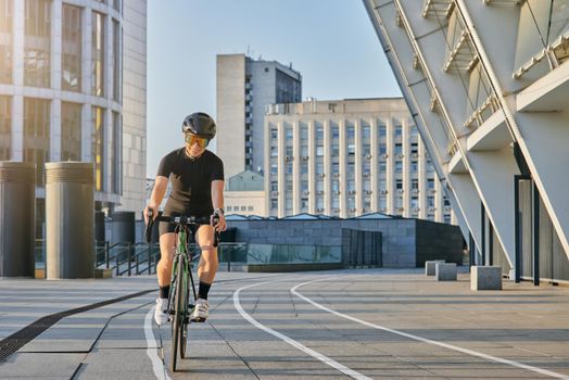 Delighted professional female cyclist in black cycling garment and protective gear smiling, looking satisfied with her training outdoors on a sunny day. Sports, active lifestyle concept