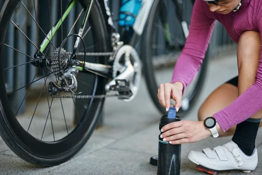 Cropped shot of young woman, professional female cyclist taking pump for inflating the tire of her bicycle, kneeling outdoors on a daytime. Transportation, sports concept