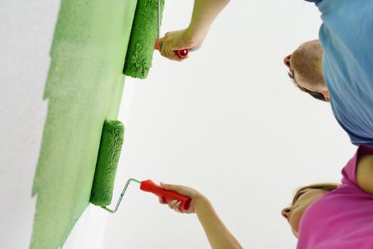 happy young couple paint in green and blue color white wall of their new home