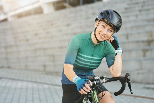 Happy professional female cyclist in protective gear smiling at camera while standing with her bike outdoors on a daytime. Active lifestyle, sports concept