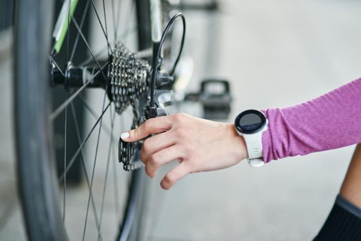 Close up shot of hand of female cyclist checking her bicycle mechanisms, sprocket and chain on a mountain bike standing outdoors on a daytime. Safety, sports, active lifestyle concept