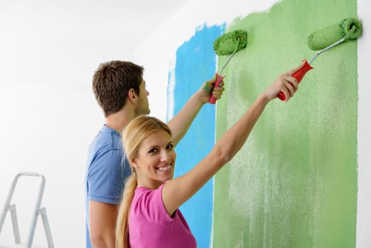 happy young couple paint in green and blue color white wall of their new home