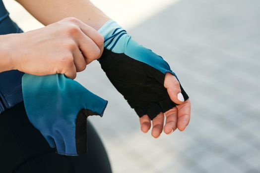 Close up shot of hands of professional female cyclist putting on cycling gloves while getting ready for training. Sports, extreme and active lifestyle concept