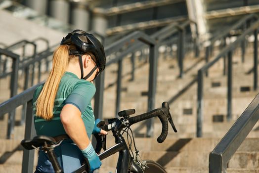Sportive young woman, professional cyclist coming up the steps with bicycle while having training outdoors. Sports, active lifestyle concept