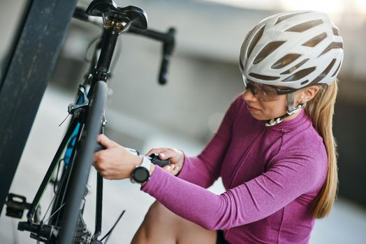 Concentrated female cyclist wearing protective helmet and glasses looking focused while using pump for inflating the tire of her bicycle, kneeling outdoors on a daytime. Transportation, sport concept