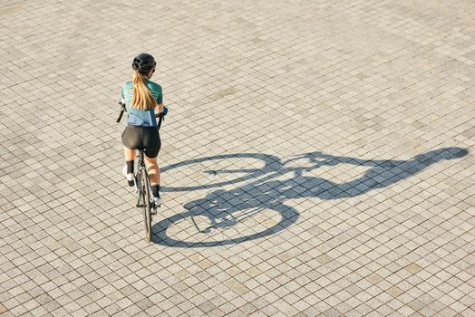Aerial view shot of professional female cyclist riding bicycle, training outdoors on a warm sunny day. Urban lifestyle, sports concept