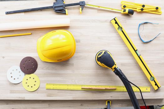 Top view of professional worker working place with equipment for work. Helmet, sander machine, level, ruler tools. Renovation, repair instrument concept