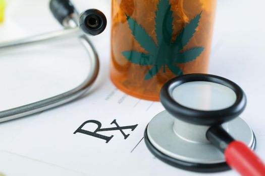 Close-up of plastic bottle with dried marijuana on blank medical prescription paper. Medication for patient, stethoscope tool. Alternative medicine concept