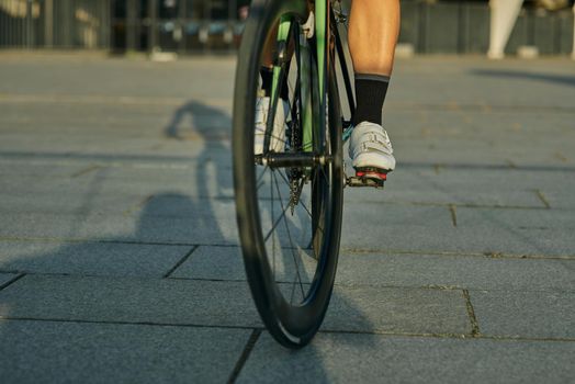 Close up shot of legs of female cyclist wearing cycling shoes riding bike in city, training outdoors on a warm day. Active lifestyle, sports concept