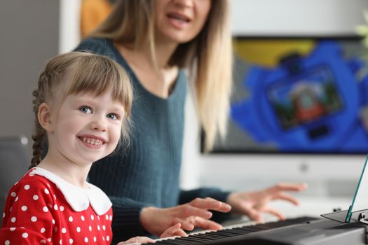 Portrait of pretty happy kid learns how to play on piano with mother. Woman artist help daughter to discover talents with music. Hobby, education concept
