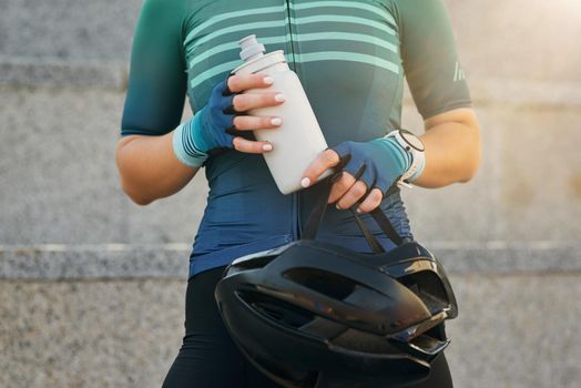 Cropped shot of young sportswoman holding black bike helmet and water bottle while getting ready for cycling. Sports, extreme and active lifestyle concept. Front view
