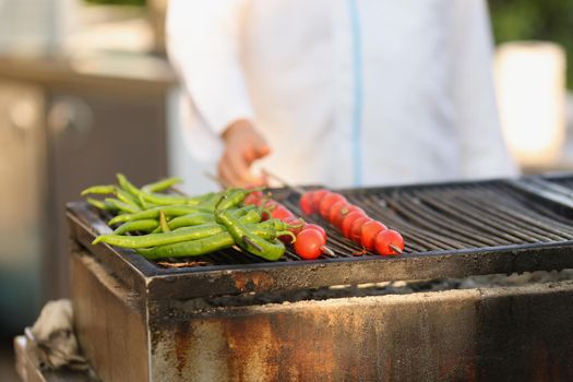 Close-up of amateur chef frying fresh tomatoes and green pepper on grill on open air. Person cooking picnic for friends. Food, cafe, eat, barbeque concept