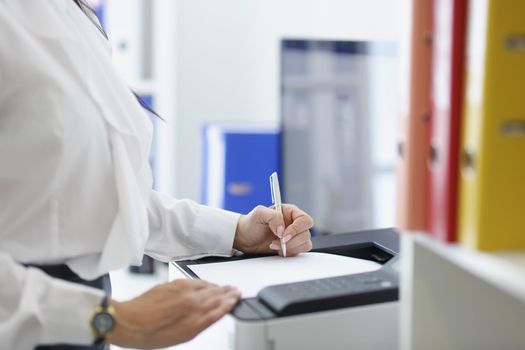 Close-up of female secretary or office worker print papers on printer machine. Company employee in suit fill document on device. Office life, job concept