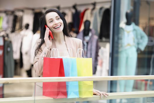 Portrait of young woman shopaholic smiling and tell to friend on call about sales. Girl carry many packs with clothes. Big sale, shopping, discount concept