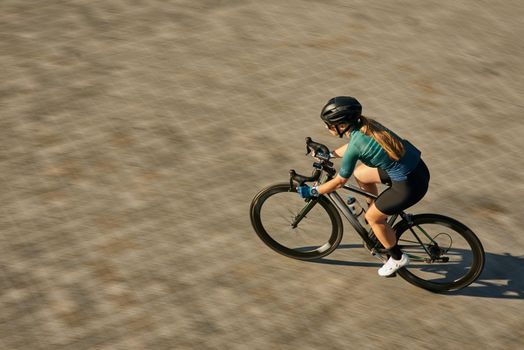 High angle view shot of professional female cyclist in cycling garment and protective gear looking focused while riding bicycle, training outdoors on a daytime. Urban lifestyle, sports concept