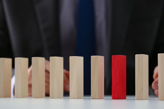 Close-up of businessman choose red wood block over simple similar wooden cubes. Dominos stand in line row. Business organization, startup, leader concept
