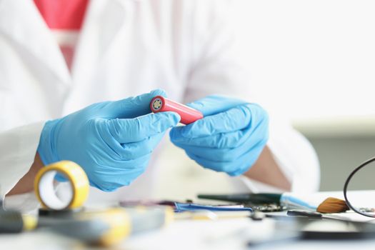 Close-up of handyman in gloves repair something electronical holding red battery detail. Man fix smartphone or motherboard. Repairman, tech, hobby concept