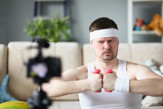 Portrait of strong middle aged man train on camera using pink dumbbells. Sportsman filming exercise or full course for social media. Blogger, sport concept