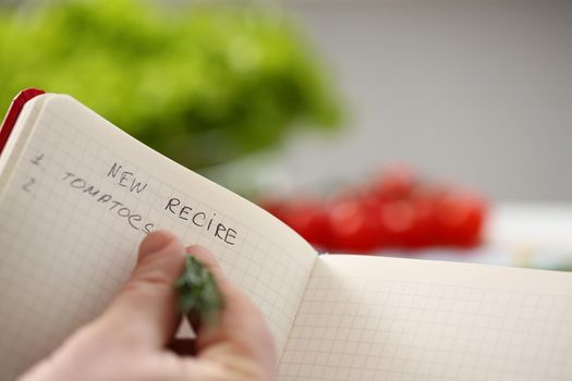 Close-up of professional chef writing down ideas for new recipe in diary. Creative cook make up new delicious meals for cooking. Food, idea, eating concept