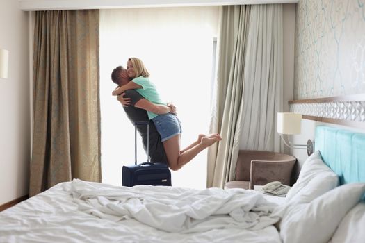 Portrait of happy wife jump in hands to husband, meet husband from work trip, warm hugs. Modern room interior, cozy bedroom. Family, relationship concept