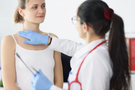 Portrait of blonde female on doctors appointment being examined by professional medical worker. Nurse touch neck and chest. Provide help, health concept