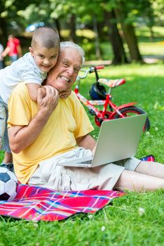 happy elderly senior grandfather and child in park using laptop computer