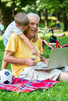 happy elderly senior grandfather and child in park using laptop computer