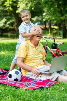 happy elderly senior grandfather and child in park using laptop computer