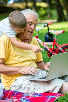 happy elderly senior grandfather and child in park using laptop computer