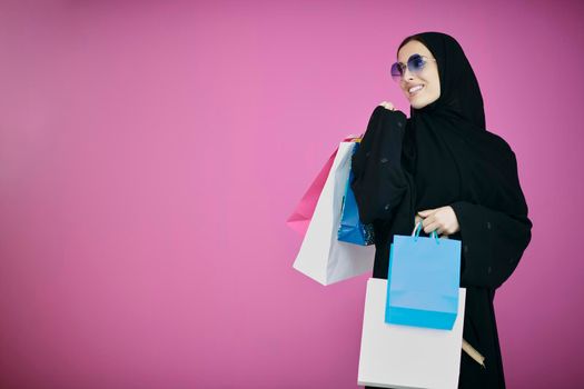 Happy muslim girl posing with shopping bags. Arabic woman wearing traditional black clothes and sunglasses representing rich and  luxurious lifestyle