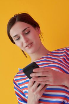 Portrait of young girl with happy face while using smartphone isolated on pink background. Female model smiling while chatting or browsing on social networks. Fashion and technology concept