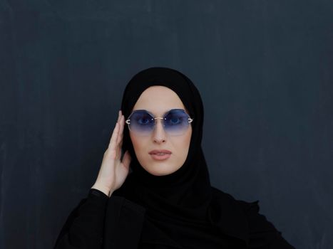 Young muslim in traditional clothes or abaya and sunglasses posing in front of black chalkboard. Arab woman representing modern arabic lifestyle, islamic  fashion and Ramadan kareem concept