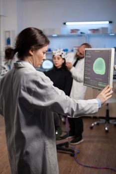 Neurologist specialist analyzing nervous system tomography on monitor while specialist doctor adjusting eeg scanner of woman patient during medical experiment. Neurology team monitoring brain activity