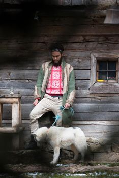 handsome young hipster man standing together with white husky dog in front of old vintage retro wooden house