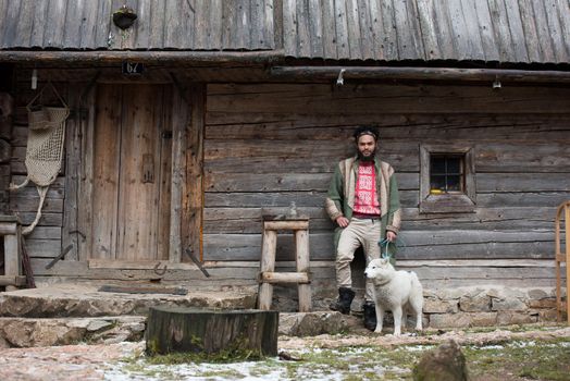 handsome young hipster man standing together with white husky dog in front of old vintage retro wooden house