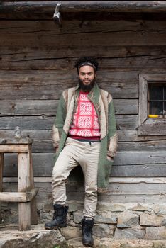 portrait of young hipster,  man with beard in front of old vintage wooden house