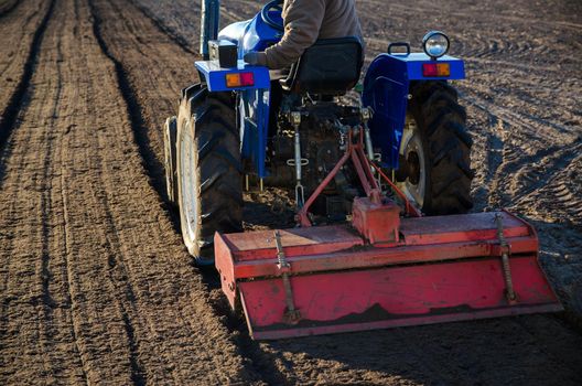A farmer on a tractor cultivates a farm field. Softening the soil and preparing for cutting rows for the next sowing season in the spring. Land cultivation. Farm business. Work in agricultural