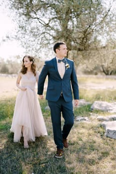 Bride and groom holding hands while walking in the park. High quality photo