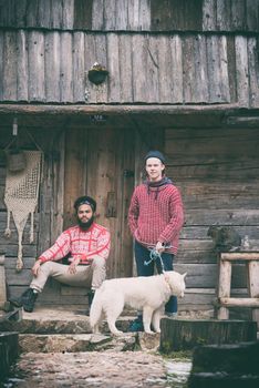 hipsters couple portrait, two young  man with white husky dog  sitting in front of old wooden retro house