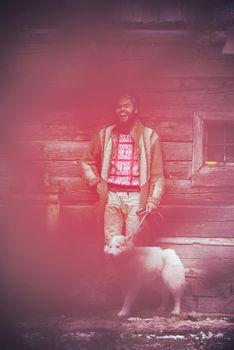 handsome young hipster man standing together with white husky dog in front of old vintage retro wooden house