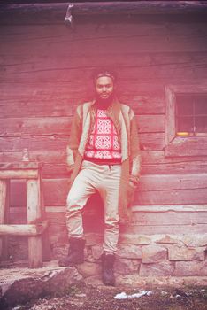 portrait of young hipster,  man with beard in front of old vintage wooden house