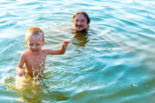 Nice moments of communication between a father and a young son - a father teaches his little son to swim in the lake, The child splashing with father, the boy is happy that he spends time with dad. High quality photo