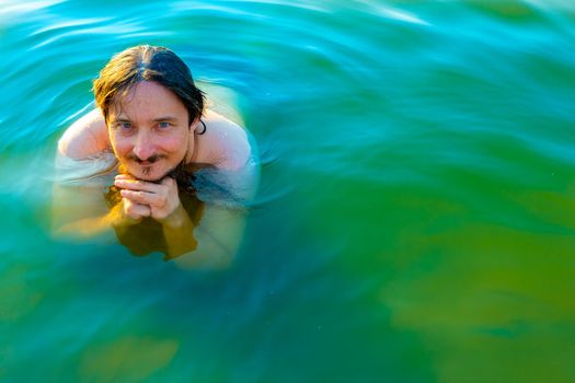 Caucasian man is swimming in a lake with blue water, lying and enjoying a summer vacation. High quality photo