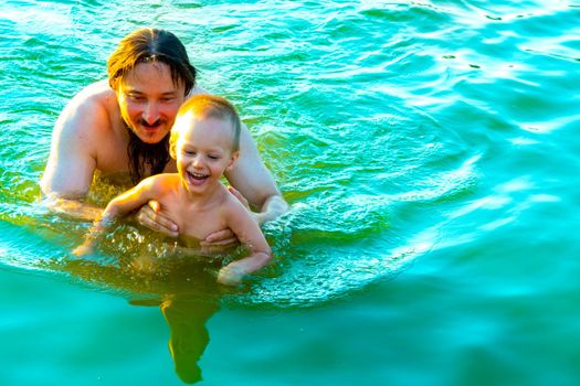 Nice moments of communication between a father and a young son - a father teaches his little son to swim in the river, hugs him and holds him tight, the boy is happy that he spends time with dad. High quality photo