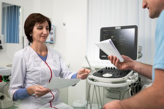 Healthcare and medicine theme. Female general practitioner will see medical tests during health examination of male patient in clinic office. Medical worker in ultrasound diagnostic room with patient.